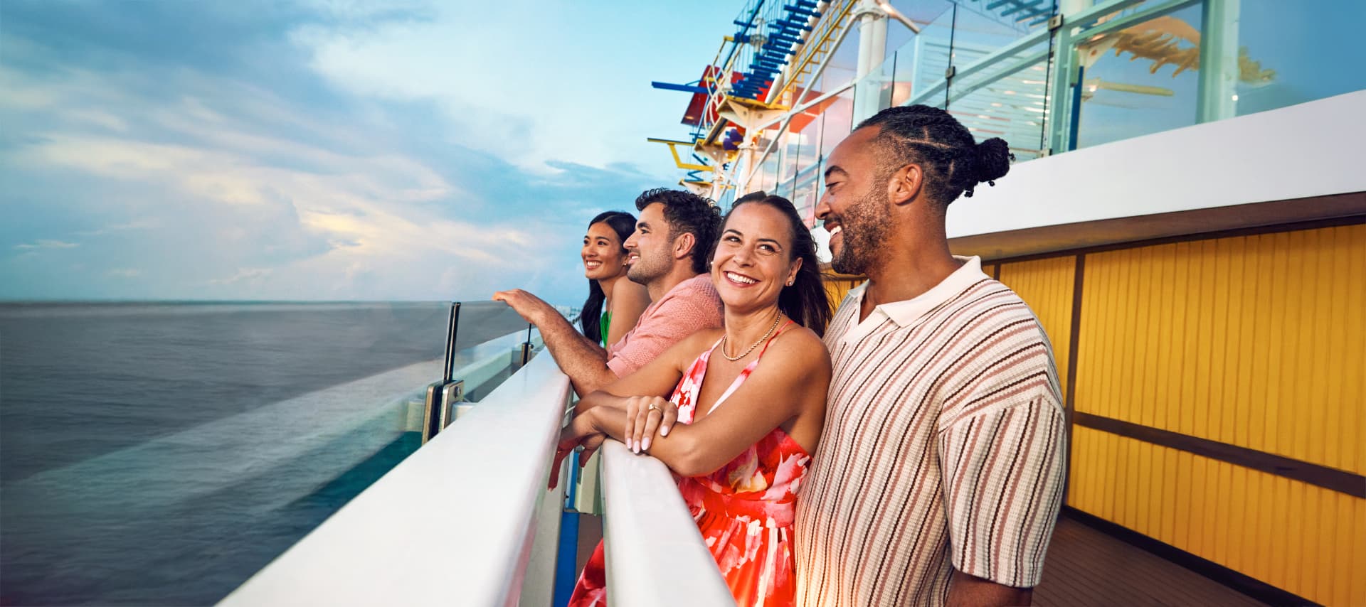 Friends laughing together at the railing of a Carnival ship at sunset