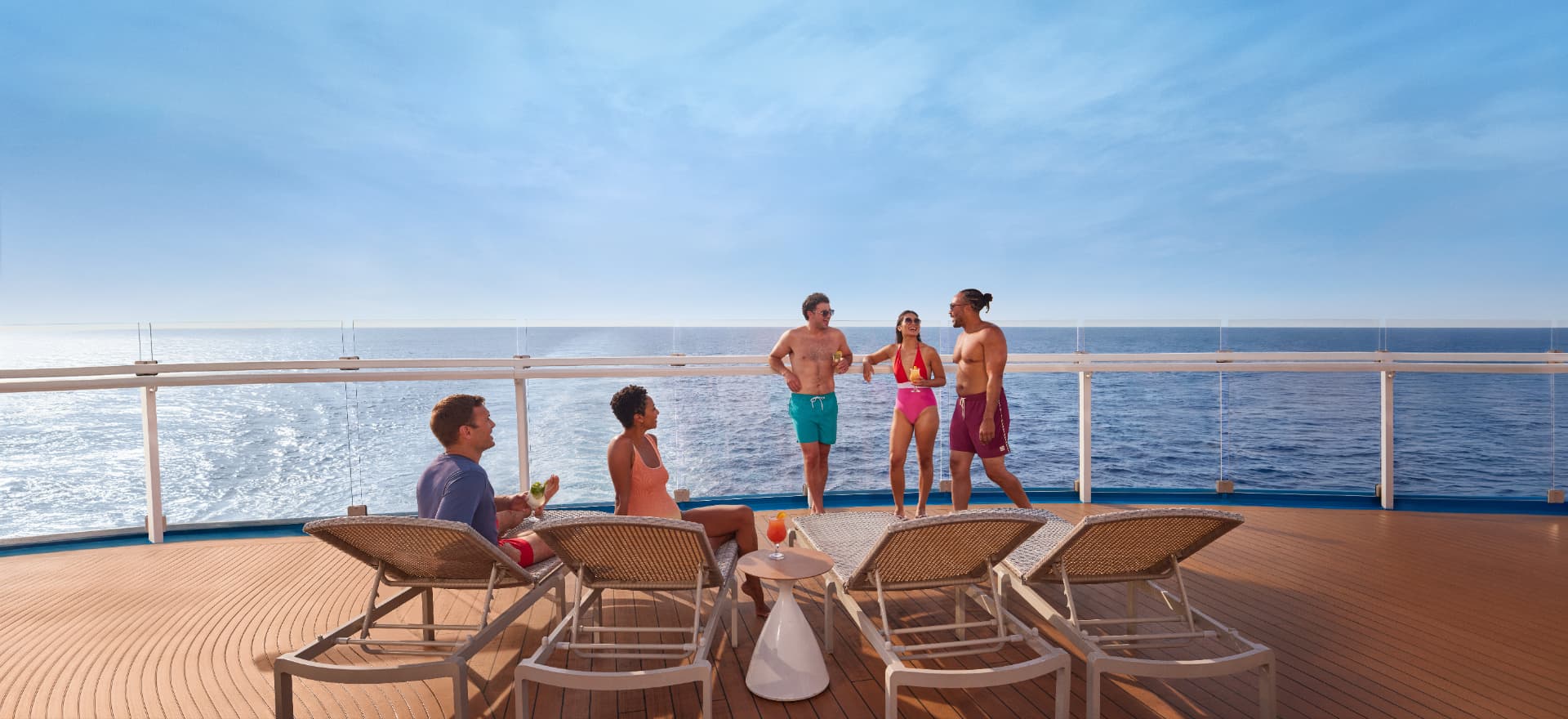 Friends relaxing on loungers at the aft deck railing of a Carnival ship at sea
