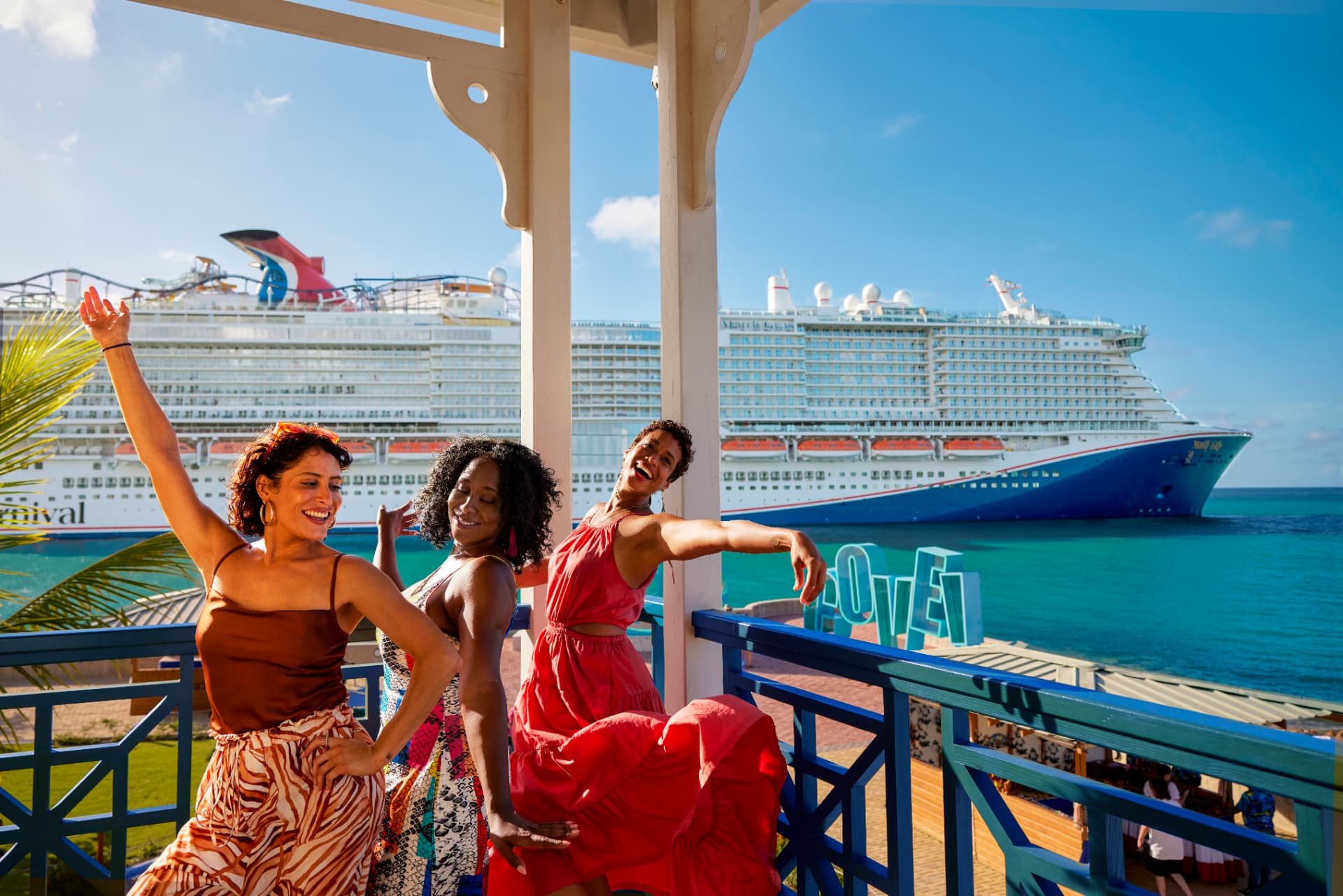 Three friends dancing in a gazebo with Carnival ships docked behind them