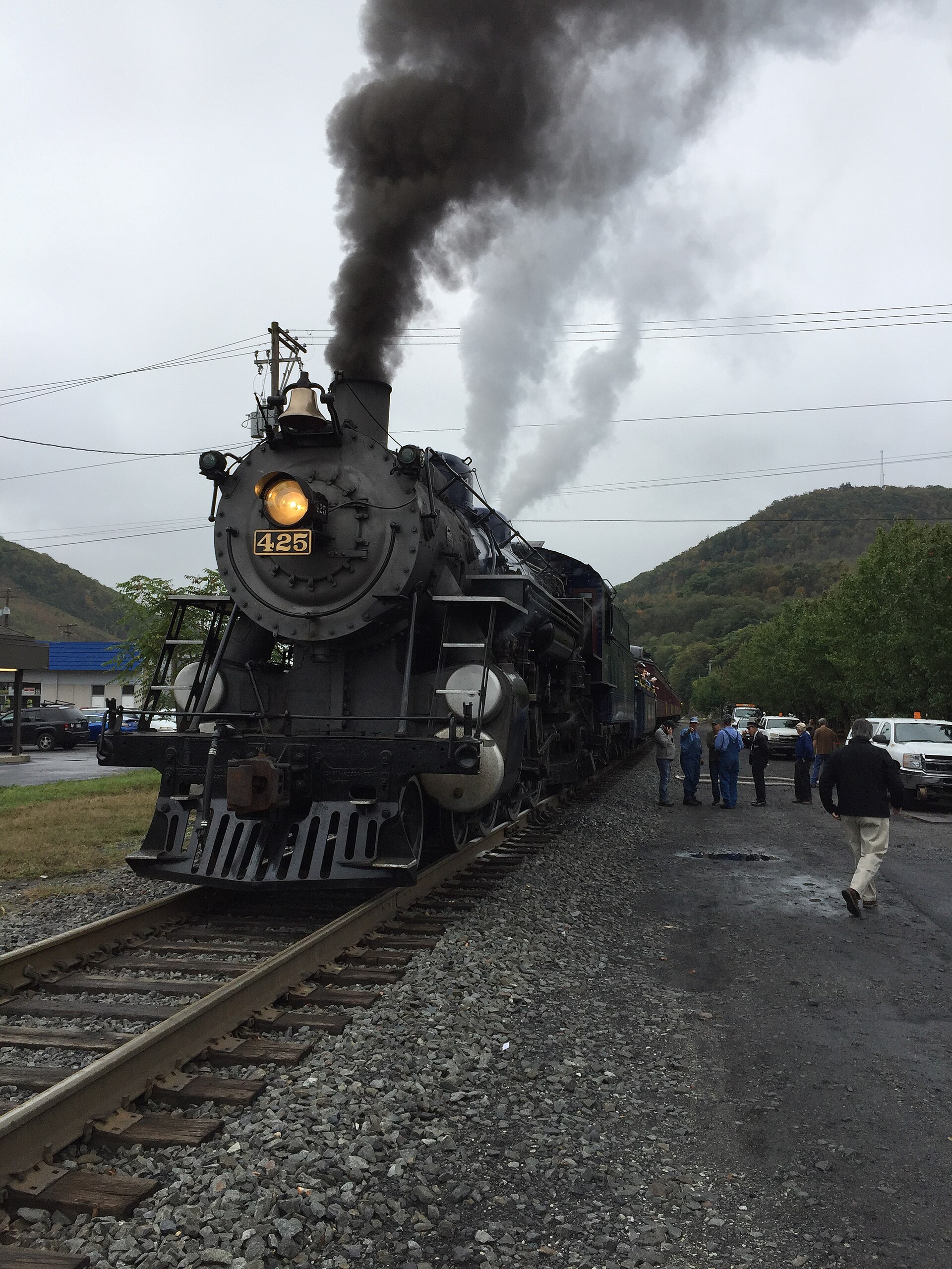 A steam locomotive pulling into the station under a plume of smoke